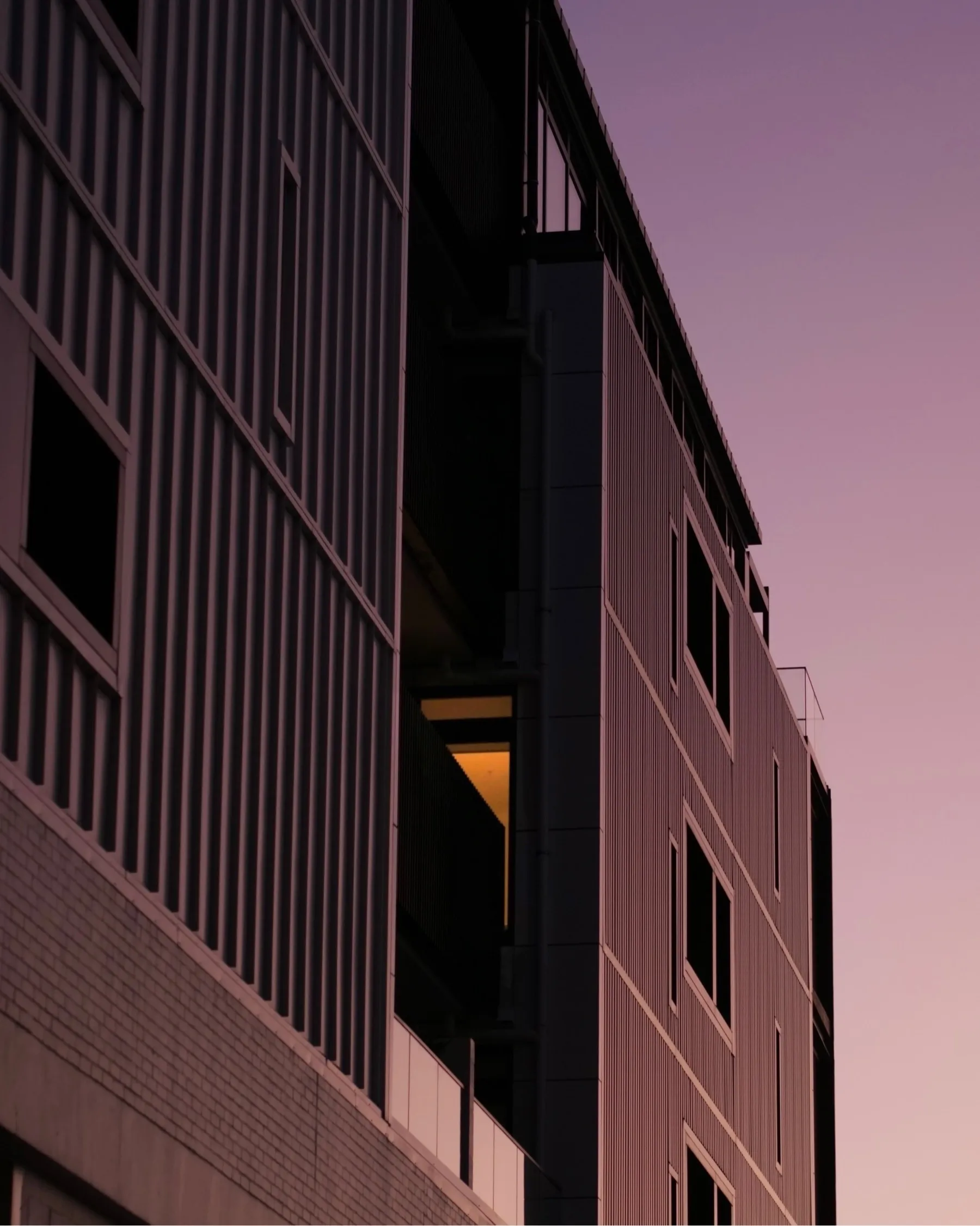 A dark grey building reflecting the violet wash of sunset
