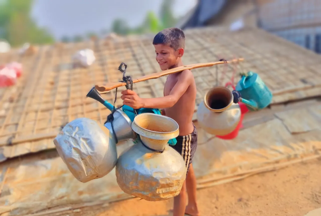A small boy carrying half a dozen water jugs on a pole