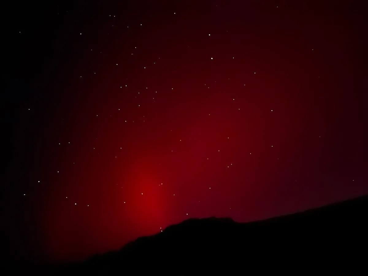 A silhouetted hill-line in front of a red aurora