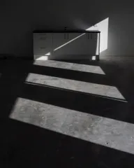 Skewed rectangles of light cutting across a shadowed concrete floor.